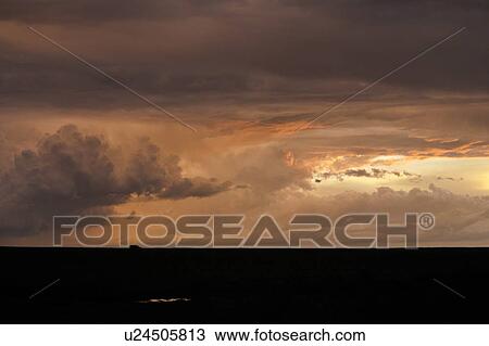 Stock Image - Dramatic orange grey swirling clouds of stormy sky on Mara plain with silhouetted safari jeep on black horizon, Masai Mara, Kenya, East Africa. Fotosearch