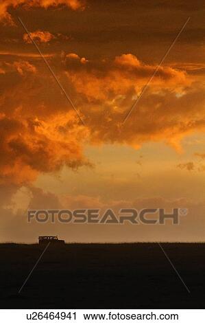 Stock Image - Dramatic orange grey swirling clouds of stormy sky on Mara plain with silhouetted safari jeep on black horizon, Masai Mara, Kenya, East Africa. Fotosearch