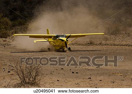 Stock Image - Front view of yellow Cessna plane at speed taking off on lake bed dust runway, Amboseli, Kenya, East Africa. Fotosearch