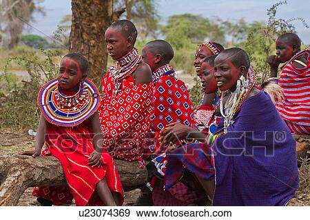 Stock Photo - Group of beautiful Masai women, all wearing colourful clothing and much beaded jewellery, sit on fallen tree trunk, waiting after face paint application, for celebrations to begin, Amboseli, Kenya, East Africa. Fotosearch
