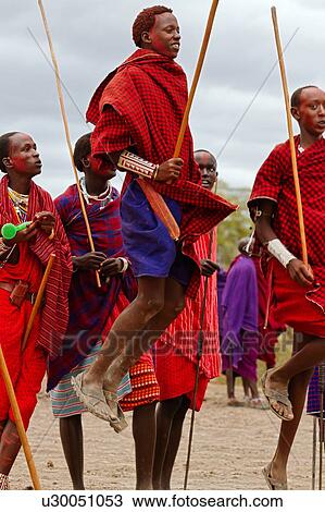 Stock Image - Masai aduma: close up of group of young Masai warriors dancing, with two jumping high in air, all holding traditional sticks, Amboseli, Kenya, East Africa. Fotosearch