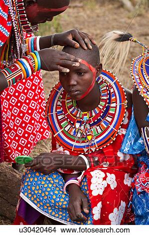 Masai applying paints for celebrations: young woman dressed in colourful clothing and much beaded jewellery sits while red paint is applied to her face by another woman, Amboseli, Kenya, East Africa View Large Photo Image Picture - Masai applying paints for celebrations: young woman dressed in colourful clothing and much beaded jewellery sits while red paint is applied to her face by another woman, Amboseli, Kenya, East Africa. Fotosearch