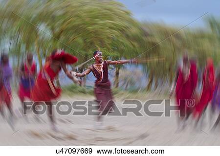Stock Photo - Masai Olympics: group of Masai warriors, all dressed in traditional red and blue shukas, stand in line for spear throwing competition, as one throws his spear, holding traditional stick for balance, motion blur effect, Amboseli, Kenya, East Africa. Fotosearch