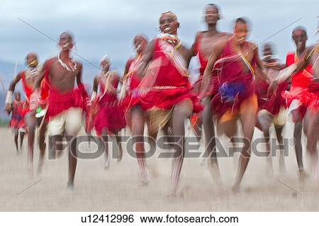 Stock Photograph - Masai Olympics: group of over 20 Masai warriors, all dressed in traditional red and blue shukas, running race on dusty plains, towards viewer, motion blur effect, Amboseli, Kenya, East Africa. Fotosearch