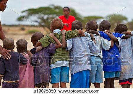 Masai school out on the plains: as seen from behind, a group of children, mostly dressed in blue sweaters, and blue form a tight line, with arms interlocked, facing their teacher dressed in red, Amboseli, Kenya, East Africa View Large Photo Image Stock Image - Masai school out on the plains: as seen from behind, a group of children, mostly dressed in blue sweaters, and blue form a tight line, with arms interlocked, facing their teacher dressed in red, Amboseli, Kenya, East Africa. Fotosearch