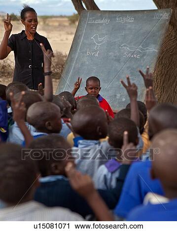 Masai school out on the plains: as seen from the back, a group of children stand in the acacia thorn enclosure in front of a blackboard under a tree, while the teacher, dressed in black, teaches them English, Amboseli, Kenya, East Africa View Large Photo Image Stock Image - Masai school out on the plains: as seen from the back, a group of children stand in the acacia thorn enclosure in front of a blackboard under a tree, while the teacher, dressed in black, teaches them English, Amboseli, Kenya, East Africa. Fotosearch