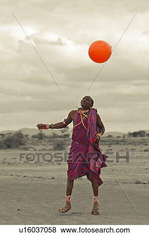 Masai warrior, dressed in traditional red and blue shuka playing with orange balloon: desaturated image, Amboseli, Kenya, East Africa View Large Photo Image Stock Photo - Masai warrior, dressed in traditional red and blue shuka playing with orange balloon: desaturated image, Amboseli, Kenya, East Africa. Fotosearch