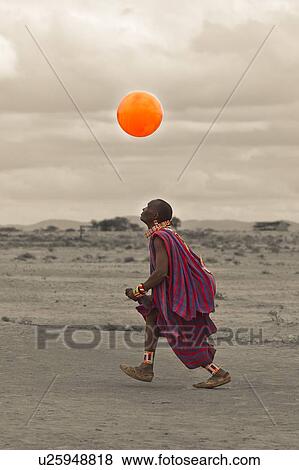 Masai warrior, dressed in traditional red and blue shuka playing with orange balloon: desaturated image, Amboseli, Kenya, East Africa View Large Photo Image Stock Photo - Masai warrior, dressed in traditional red and blue shuka playing with orange balloon: desaturated image, Amboseli, Kenya, East Africa. Fotosearch