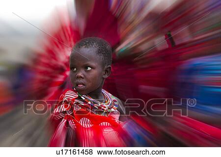 Stock Photo - Portrait of young Masai child, dressed in colourful traditional red and white cotton wrap, and beaded jewellery, front side view, with radial blur effect, Amboseli, Kenya, East Africa. Fotosearch
