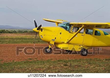Picture - Side view of yellow Cessna plane on dirt runway, Masai Mara, Kenya, East Africa. Fotosearch