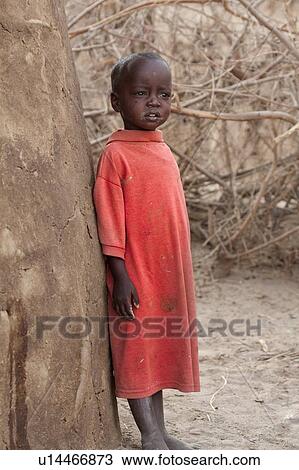Small Masai child wearing long red T-shirt standing leaning against mud house, with acacia thorn fencing in background, Masai village, Amboseli, Kenya, East Africa View Large Photo Image Stock Image - Small Masai child wearing long red T-shirt standing leaning against mud house, with acacia thorn fencing in background, Masai village, Amboseli, Kenya, East Africa. Fotosearch