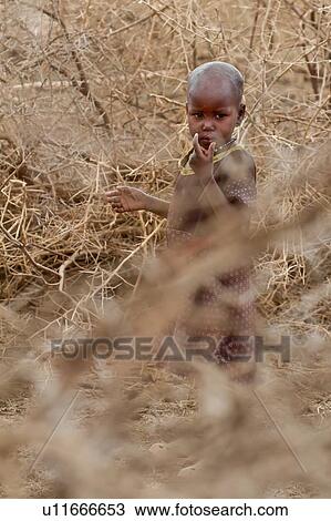 Stock Image - Small Masai girl standing framed by acacia thorn fencing, close up, Amboseli, Kenya, East Africa. Fotosearch