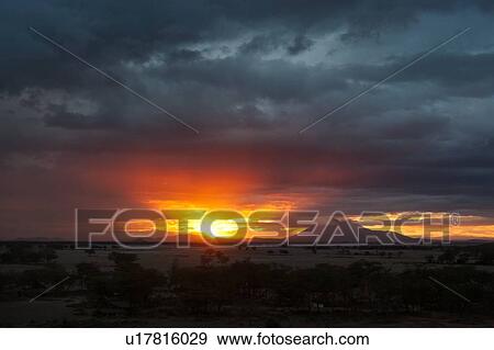 Sunset at Amboseli: dramatic red orange yellow against stormy grey clouds, over distant mountain, sandy plains and trees in foreground, Amboseli, Kenya, East Africa View Large Photo Image Stock Photo - Sunset at Amboseli: dramatic red orange yellow against stormy grey clouds, over distant mountain, sandy plains and trees in foreground, Amboseli, Kenya, East Africa. Fotosearch