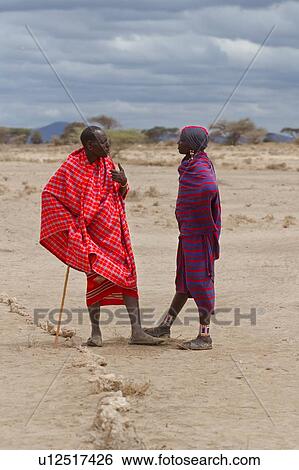 Two Masai men, older one leaning on traditional stick, standing talking in open plains, Amboseli, Kenya, East Africa View Large Photo Image Stock Photograph - Two Masai men, older one leaning on traditional stick, standing talking in open plains, Amboseli, Kenya, East Africa. Fotosearch