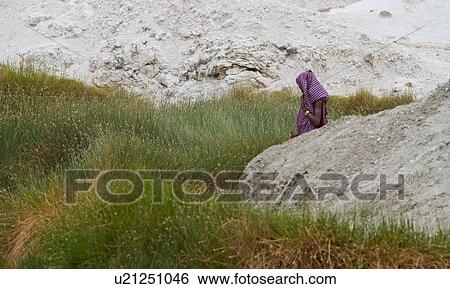 Young Masai man with head covered by red and blue shuka stands in green reeds near Amboseli lake bed, framed by rocky slopes, Amboseli, Kenya, East Africa View Large Photo Image Stock Photograph - Young Masai man with head covered by red and blue shuka stands in green reeds near Amboseli lake bed, framed by rocky slopes, Amboseli, Kenya, East Africa. Fotosearch