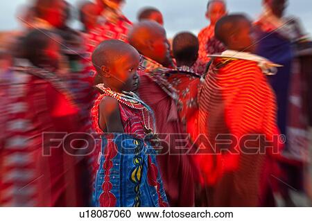 Stock Image - Young Masai women stand in golden evening sunlight, dressed in colourful red and white wraps, with much beaded jewellery, and painted faces for celebrations, portrait of child with blur effect, Amboseli, Kenya, East Africa. Fotosearch