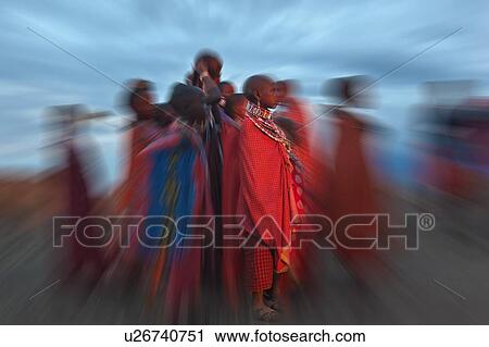 Stock Image - Young Masai women stand in golden evening sunlight, dressed in colourful red and white wraps, with much beaded jewellery, and painted faces for celebrations, portrait with radial blur effect, Amboseli, Kenya, East Africa. Fotosearch