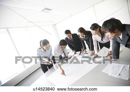 Stock Image - Businesspeople examining Blueprint in Meeting. Fotosearch