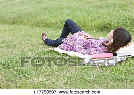 Stock Photo - Female Student Lying on Grass and Listening to Headphones. Fotosearch