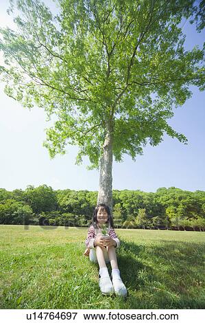 Stock Photo - Girl holding a potted plant leaning on a tree. Fotosearch