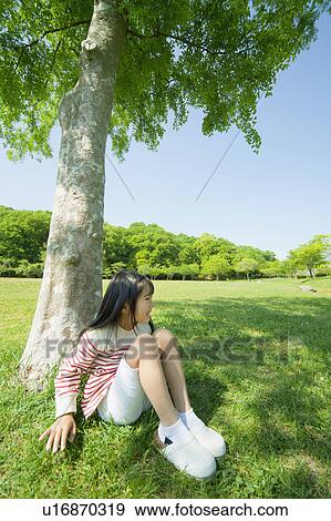 Girl sitting under a tree View Large Photo Image Stock Photo - Girl sitting under a tree. Fotosearch