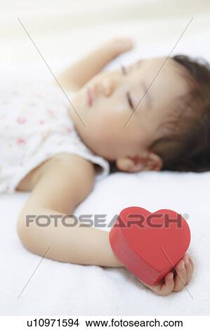 Picture - Girl sleeping holding a heart shape toy. Fotosearch