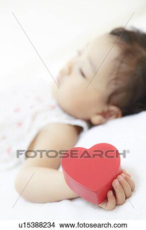 Picture - Girl sleeping holding a heart shape toy. Fotosearch