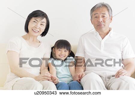 Stock Image - Grandparents and Granddaughter Holding Hands on Sofa. Fotosearch