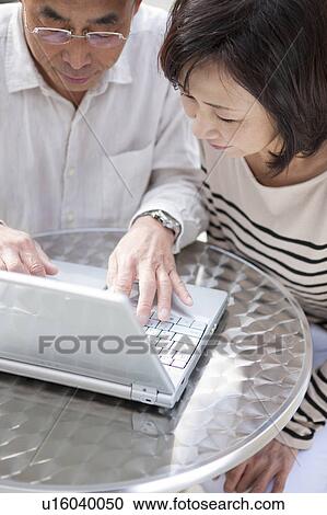 Stock Image - Mature couple using laptop outdoors. Fotosearch