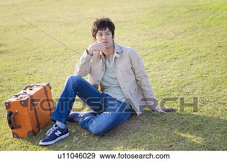 Stock Photo - Mid Adult Man With Suitcase Sitting on Grass. Fotosearch