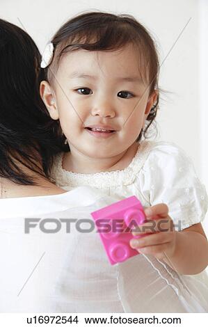 Mother carrying daughter who's holding a plastic block View Large Photo Image Picture - Mother carrying daughter who's holding a plastic block. Fotosearch