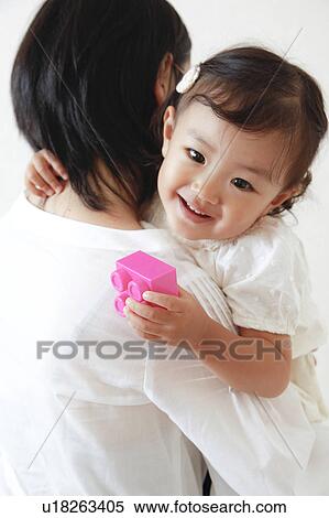 Stock Photography - Mother carrying daughter who's holding a plastic block. Fotosearch