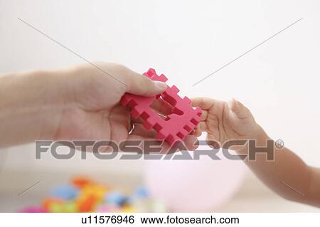 Stock Photograph - Mother giving a piece of puzzle to daughter. Fotosearch