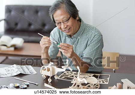 Stock Photography - Senior Man Painting Wooden Models. Fotosearch