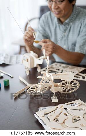 Stock Photography - Senior Man Painting Wooden Models. Fotosearch