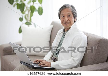 Stock Photo - Senior Man Using Laptop on Sofa. Fotosearch