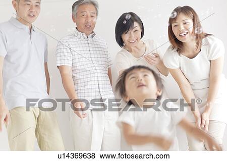Stock Photo - Three Generation Family, Boy in Foreground Playing With Bubbles. Fotosearch
