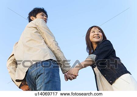Stock Photo - Young Couple Holding Hands and Looking Back. Fotosearch