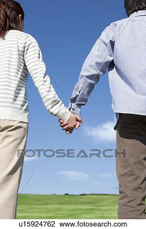 Stock Image - Young Couple Holding Hands in Field. Fotosearch