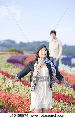 Picture - Young Woman in Field of Flowers, Man in Background. Fotosearch