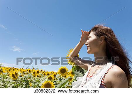 Stock Image - Young Woman Shielding Eyes in Field. Fotosearch