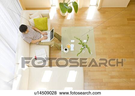 Stock Photo - Man in living room using laptop. Fotosearch