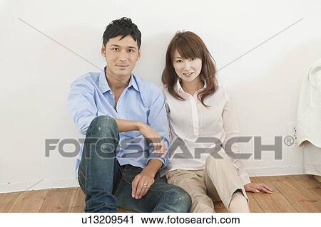 Stock Image - Portrait of young couple sitting on floor. Fotosearch