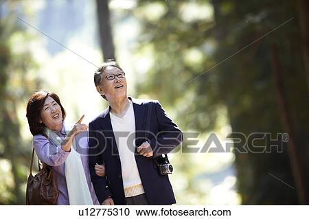 Stock Image - Senior Couple Walking in Park and Pointing. Fotosearch