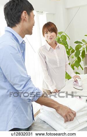 Stock Image - Young couple folding laundry and ironing. Fotosearch