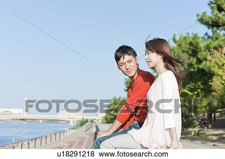 Stock Photo - Young couple sitting by river, Hyogo Prefecture, Honshu, Japan. Fotosearch