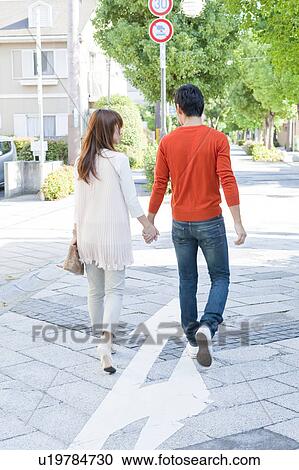 Stock Image - Young couple walking holding hands. Fotosearch