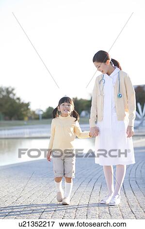 Stock Photo - Young Female Nurse and Girl Walking Hand in Hand. Fotosearch