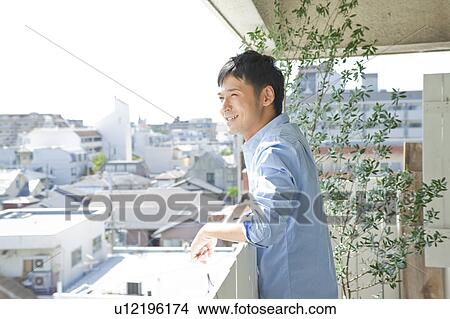 Picture - Young man looking out the balcony. Fotosearch