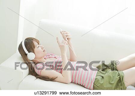 Young woman listening to music on sofa View Large Photo Image Stock Photo - Young woman listening to music on sofa. Fotosearch